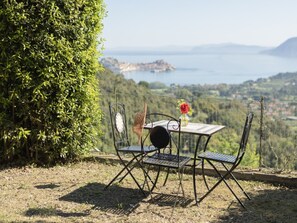 Une table et des chaises sont disposées à l’extérieur, offrant une vue sur une étendue d’eau et des collines en arrière-plan.