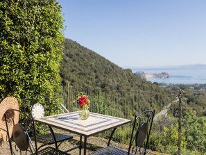 Une table et des chaises installées à l’extérieur, un vase avec une fleur rouge, et une vue sur un paysage montagneux.