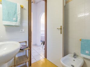 Une salle de bain avec un grand lavabo, un plus petit lavabo, un porte-serviettes et une porte donnant sur un balcon.