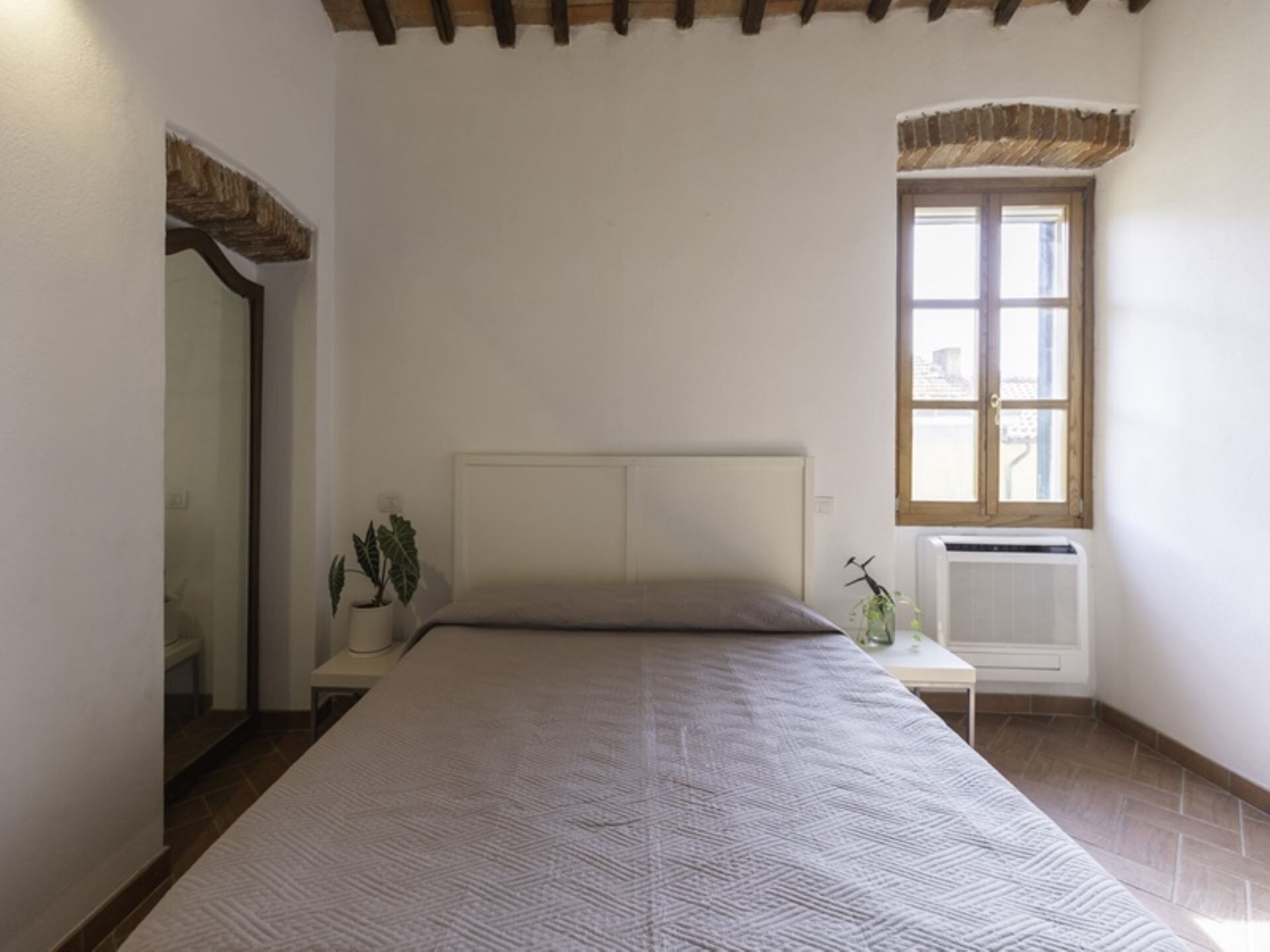 Un dormitorio con una cama grande, una ventana con vistas, un radiador y una planta en la mesita de noche.