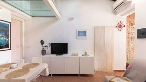 A modern living room with a TV, white cabinets, a glass table, and a brick wall. - In the heart of Portoferraio's historic center! (Portoferraio)