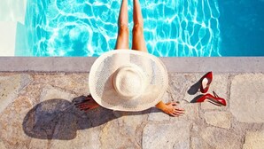 En person ligger ved en stenskønt pool med en stråhat og røde højhæle ved siden af.
