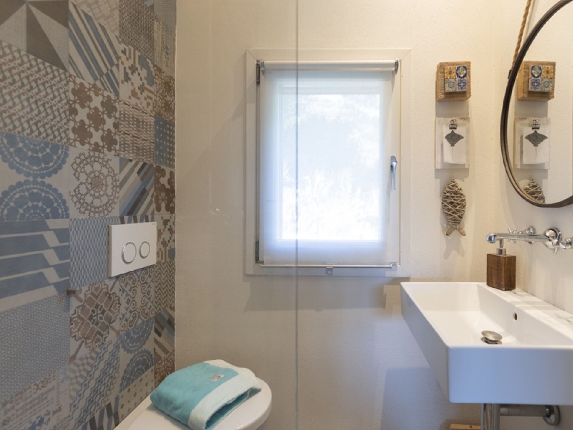 A bathroom with a patterned wall, a toilet, a window, a sink, and a mirror.