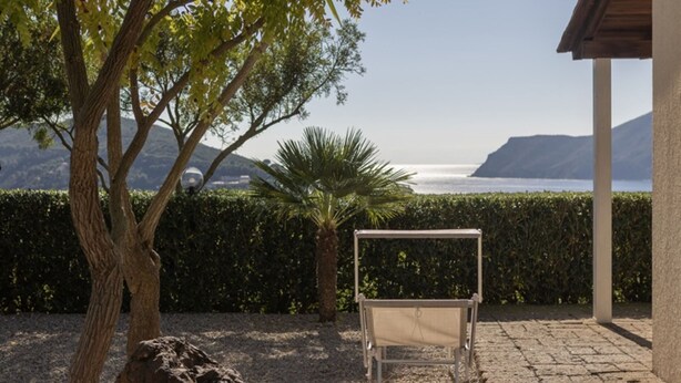 A serene outdoor seating area with a view of the sea and mountains, a palm tree, and a rock. - Fantastic sea view and privacy (Lacona)