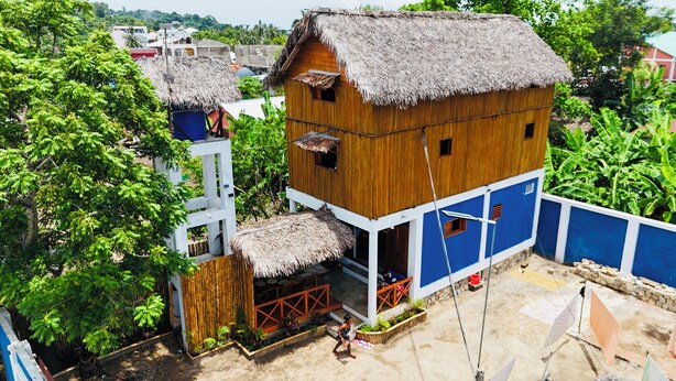 Een houten huis met rieten dak, omgeven door weelderige begroeiing.