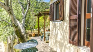 Un pati empedrat amb mobiliari exterior, una pèrgola i vista a un jardí exuberant.