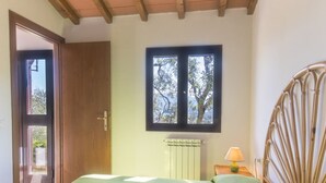 Habitació amb un llit, una finestra amb vistes a arbres, un radiador i una porta de fusta.