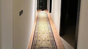 Un pasillo con alfombra estampada, una lámpara en el techo y una puerta al final.