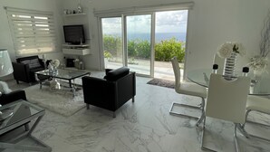A modern living room with a TV, seating, and a view of the outdoors. - Modern Ocean View Apartment (Pointe Blanche)