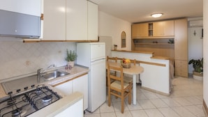 A compact kitchen with white cabinets, a gas stove, a sink, and a small dining area with a chair and table. - Quiet, well-kept stay for couples or families (Campo nell'Elba)