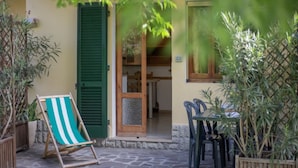 A stone-floored patio with a wooden table and chairs, a striped beach chair, and a wooden door with green shutters. - Quiet, well-kept stay for couples or families (Campo nell'Elba)