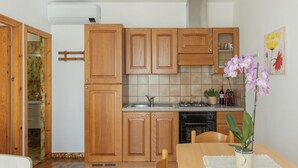 A kitchen with wooden cabinets, a stove, and a sink. There is a dining table with chairs and a vase of flowers. - One-bedroom apartment with garden & Lacona view (Lacona)