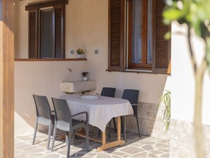 Un patio al aire libre con una mesa y sillas, piso de piedra, contraventanas de madera y plantas en macetas.