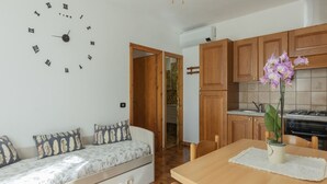 A cozy room with a bed, a dining table, a wooden cabinet, and a wall clock. - One-bedroom apartment with garden & Lacona view (Lacona)
