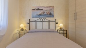 A bedroom with a bed, two bedside tables with lamps, a painting on the wall, and a wardrobe. - One-bedroom apartment with garden & Lacona view (Lacona)