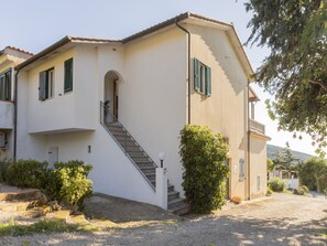 A two-story house with a staircase leading to the entrance, surrounded by greenery and a gravel driveway. - Large terrace with view over the Gulf of Lacona (Lacona)