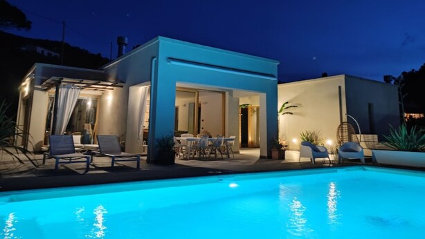 A modern house with a swimming pool, outdoor seating, and a well-lit patio area.