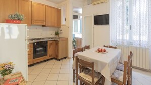 A compact kitchen with wooden cabinets, a stove, and a dining area with a table set for two. - In the center, 100 meters from the sea! (Marina di Campo)