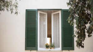 A window with green shutters, a small balcony with potted plants, and a view of a building with a white facade. - In the center, 100 meters from the sea! (Marina di Campo)