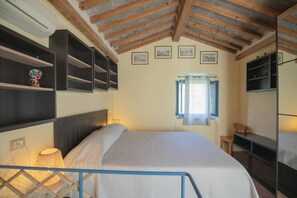 A bedroom with a bed, a window, a shelf with decorative items, and a TV. - Perfect for couples, independent and on two levels (Rio Marina)