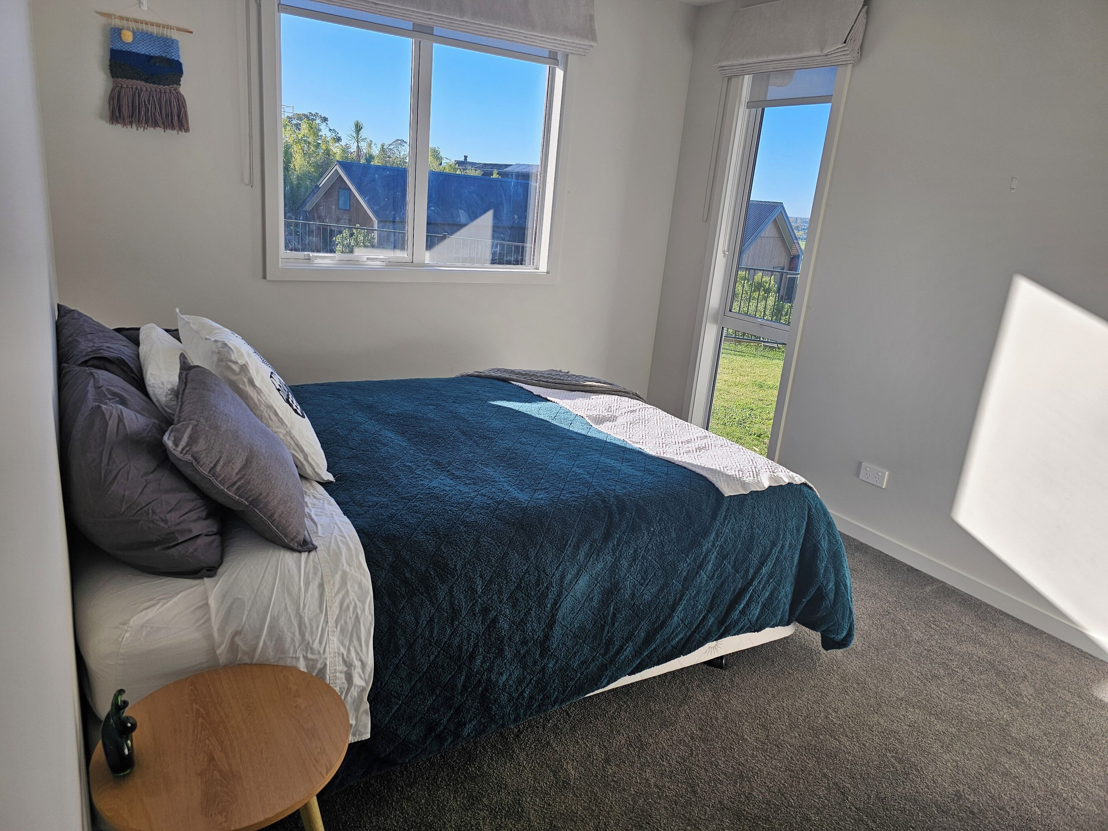 A bedroom with a bed, a small wooden table, and a window with a view of houses.