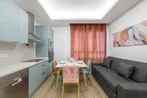 Eine kompakte Küche mit Essbereich, einem grauen Sofa und abstrakter Wandkunst.