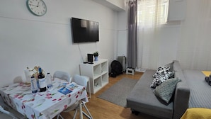 A compact living space with a dining table, sofa, TV, and a small shelf with items. - Basement apartment studio in Lisbon Portugal, near the center. (Lisboa)