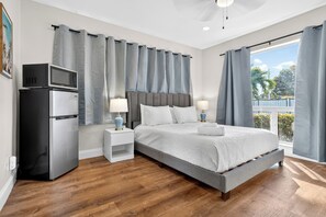 A bedroom with a bed, two bedside tables with lamps, a microwave, and a refrigerator. - Swaying Palms Unit 1: 2 BR 2 Bath Retreat, Near Beach, Heated Pool, Free Parking (Fort Lauderdale)