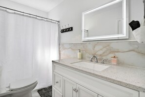 A bathroom with a white toilet, a marble sink vanity, a large mirror, and a shower curtain. - Swaying Palms Unit 1: 2 BR 2 Bath Retreat, Near Beach, Heated Pool, Free Parking (Fort Lauderdale)