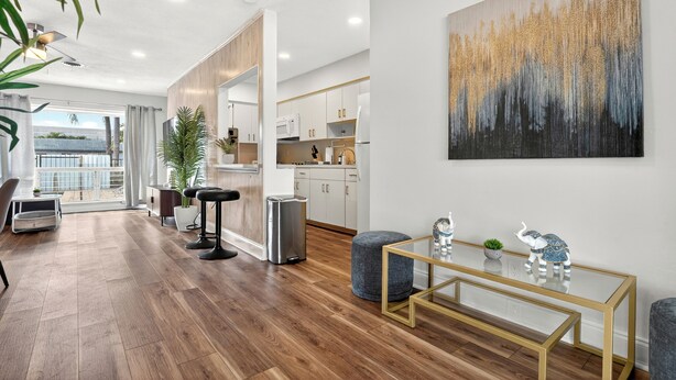 A modern living room with a wooden floor, a glass coffee table, and a large abstract painting. - Swaying Palms Unit 1: 2 BR 2 Bath Retreat, Near Beach, Heated Pool, Free Parking (Fort Lauderdale)
