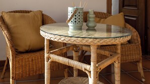 A wicker chair with a cushion, a glass table with a woven base, and a decorative container with sticks. - Rural house for 15 people in Alcover, Nature, mountain and beach very close. (La Plana)