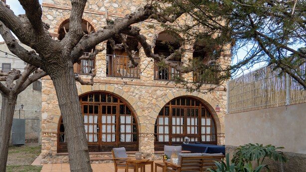A stone building with arched windows and a patio area with outdoor furniture. - Rural house for 15 people in Alcover, Nature, mountain and beach very close. (La Plana)