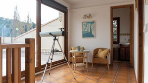 Ein Balkon mit Teleskop, Korbmöbeln und Blick auf Bäume.