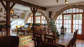 A cozy dining area with a wooden table and chairs, surrounded by stone arches and large windows. - Rural house for 15 people in Alcover, Nature, mountain and beach very close. (La Plana)