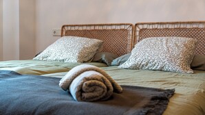 A bed with a woven headboard, patterned pillows, and a rolled towel on a textured blanket. - Rural house for 15 people in Alcover, Nature, mountain and beach very close. (La Plana)