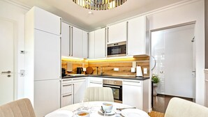 Una cocina moderna con armarios blancos, horno empotrado y comedor con una mesa y sillas de mármol.