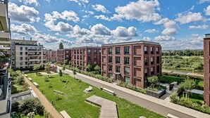 Un moderno complejo de apartamentos con un patio central, edificios de ladrillo y un río al fondo.