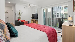 Quarto de hotel moderno com uma cama grande, uma escrivaninha, uma TV e uma varanda com vista para a cidade.