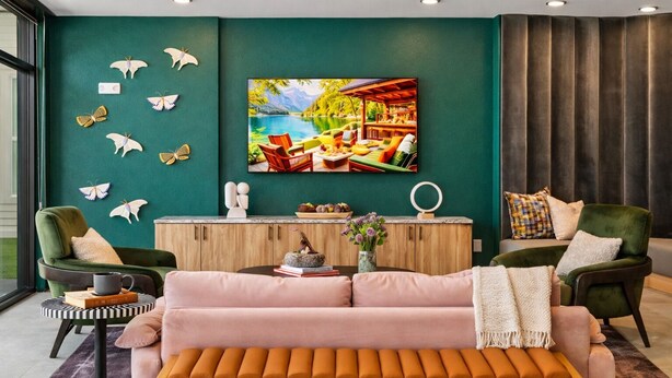 Uma sala de estar moderna com uma parede de destaque azul-turquesa, uma televisão de tela plana grande e uma área de estar aconchegante com um sofá rosa e poltronas verdes.