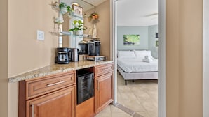 A kitchen with a granite countertop, built-in dishwasher, and coffee makers. There is a bed visible through an open door in the adjacent room. - Oceanfront Balcony Views at Dolphin Sightings (North Topsail Beach)