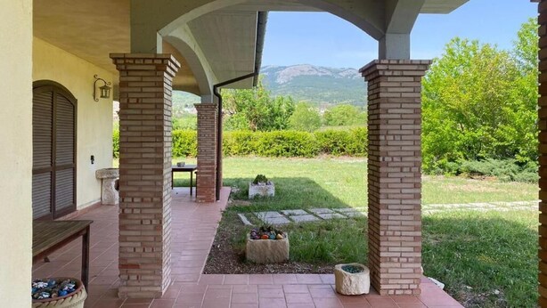 A covered outdoor area with brick pillars, a stone pathway, and a view of a green landscape with mountains in the distance. - Agriturismo C'era Una Volta (Poggio Picenze)