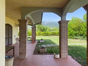 A covered outdoor area with brick pillars, a stone pathway, and a view of a green landscape with mountains in the distance. - Agriturismo C'era Una Volta (Poggio Picenze)