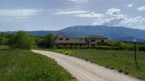 A rural road leading to a two-story house with a gravel driveway. - Agriturismo C'era Una Volta (Poggio Picenze)