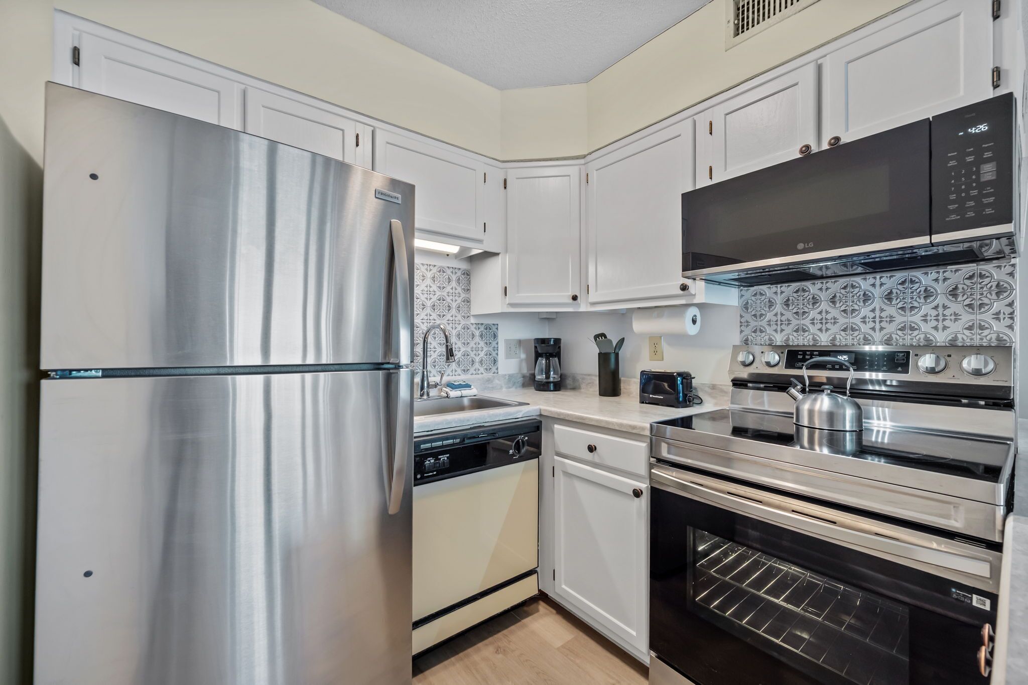 A modern kitchen with stainless steel appliances, white cabinetry, and patterned backsplash tiles.