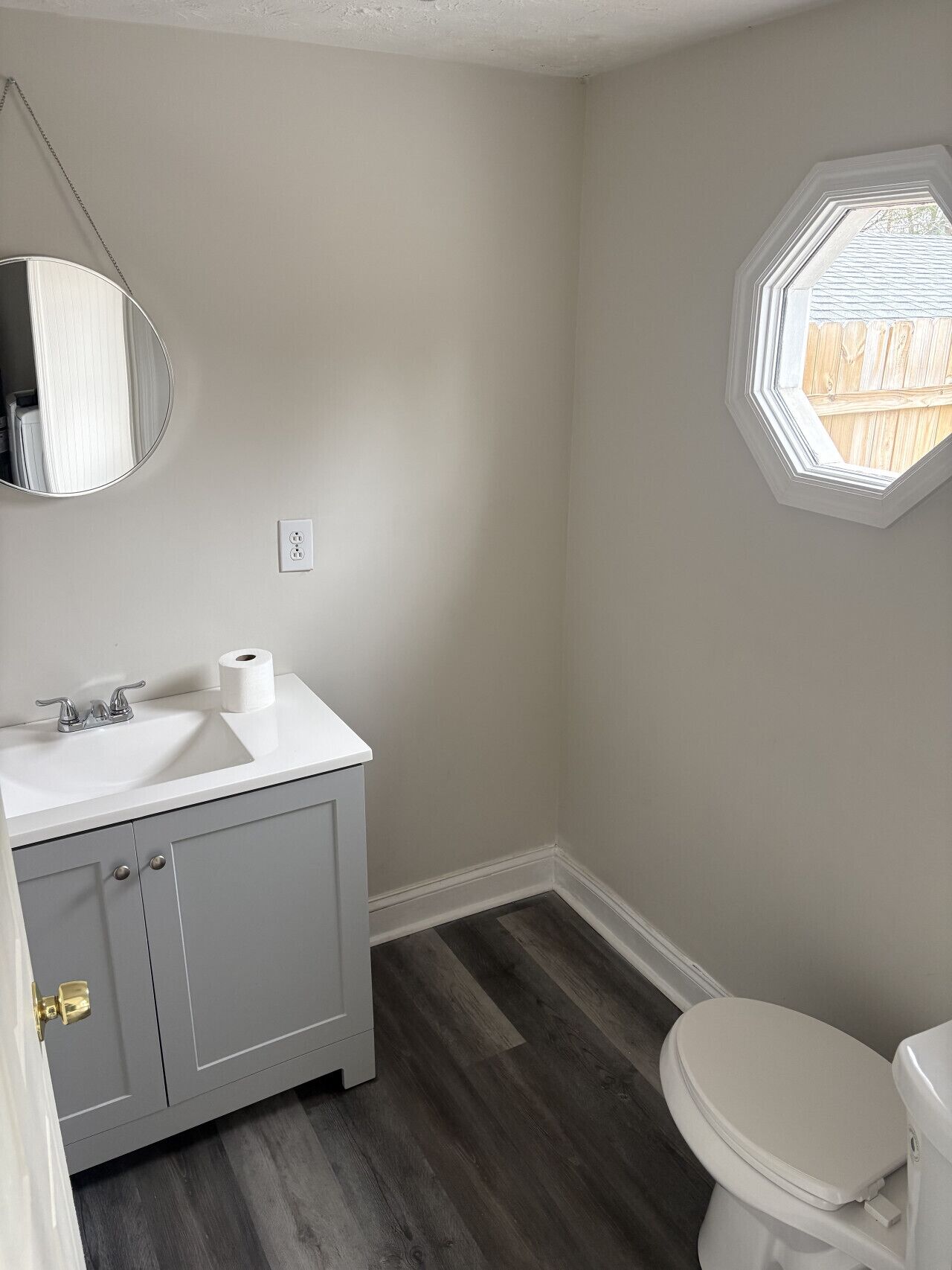 Une salle de bain avec un lavabo blanc, des toilettes et une fenêtre donnant sur une clôture en bois.