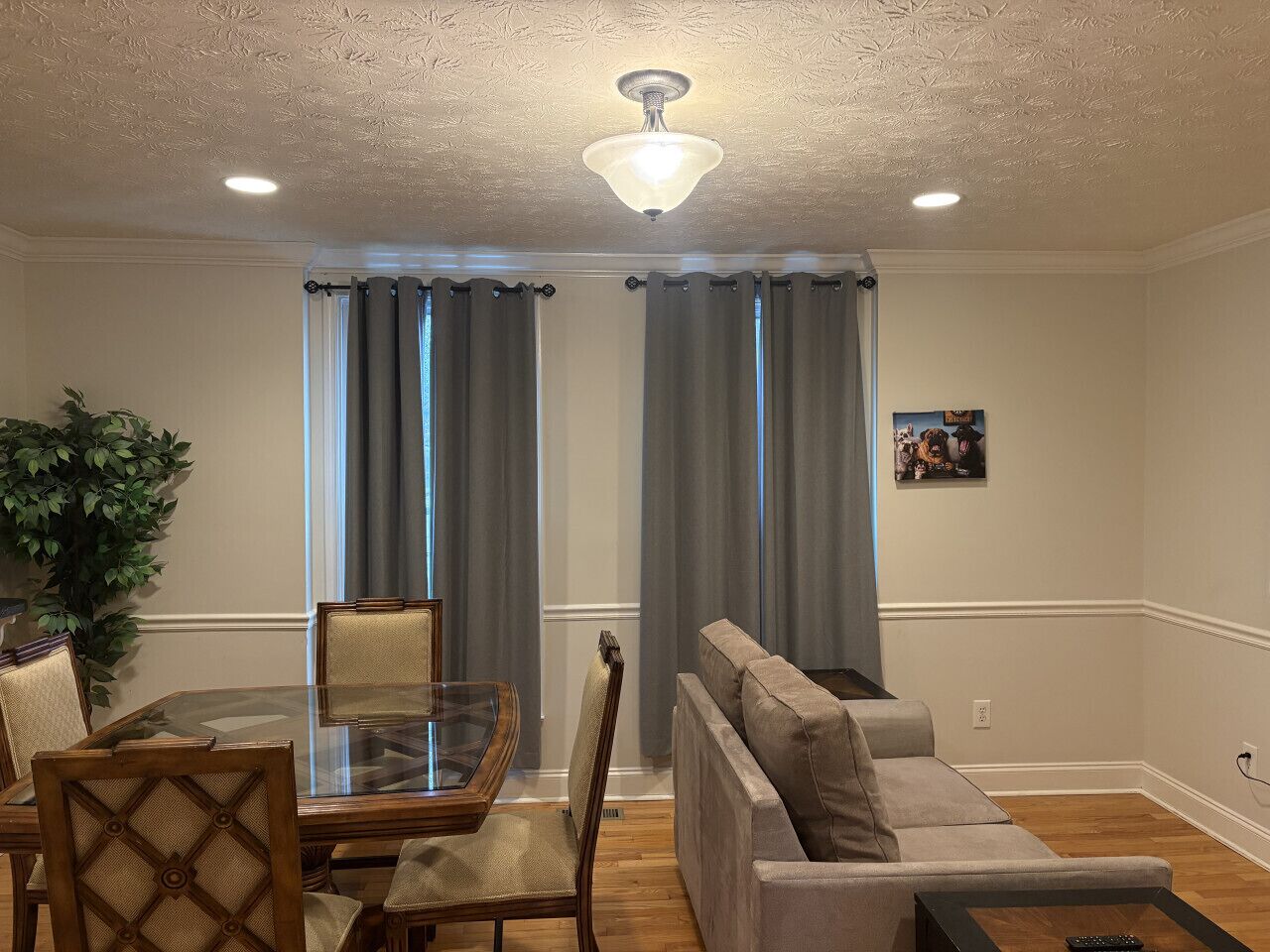 A living room with a glass-top dining table, cushioned chairs, a sofa, and a ceiling fan.