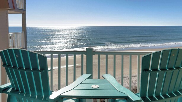 Un balcone con vista sull'oceano, con due poltrone Adirondack verdi e un tavolino.