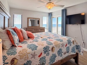 Ein Schlafzimmer mit einem Bett, einem Deckenventilator, einem Schminktisch, einem Fernseher und Meerblick durch große Fenster.