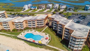 Un hotel a più piani con area piscina centrale, circondato da parcheggio e spiaggia.