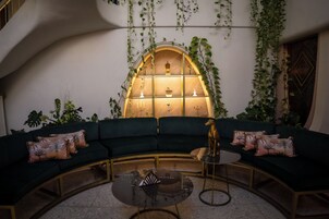 Un sofá verde curvado con cojines estampados, una mesa de centro de vidrio y una estatua decorativa de un perro.